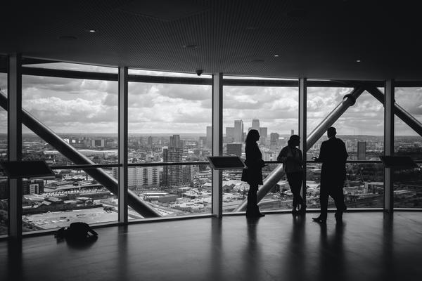 Three adults stand on the top floor of a building, looking over the city