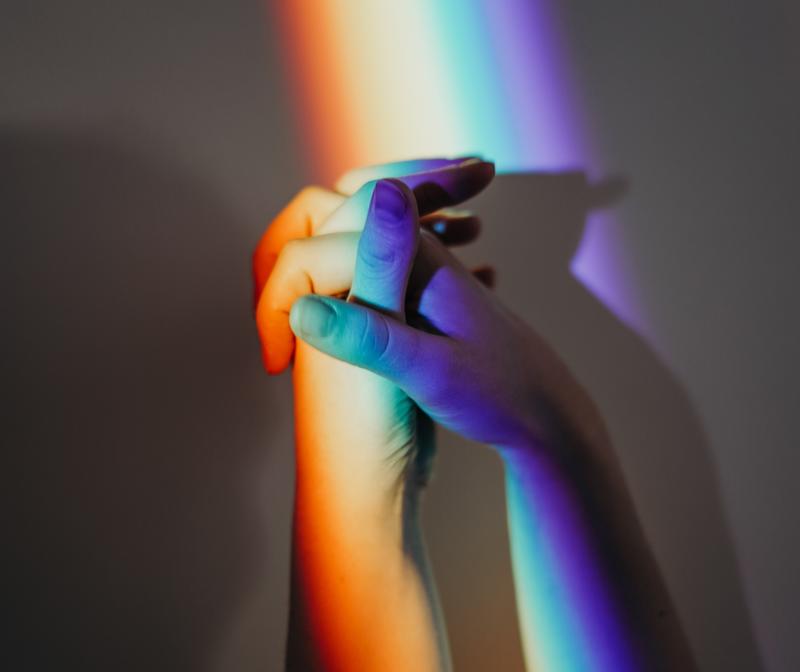 Close-up image of two hands in rainbow coloured light
