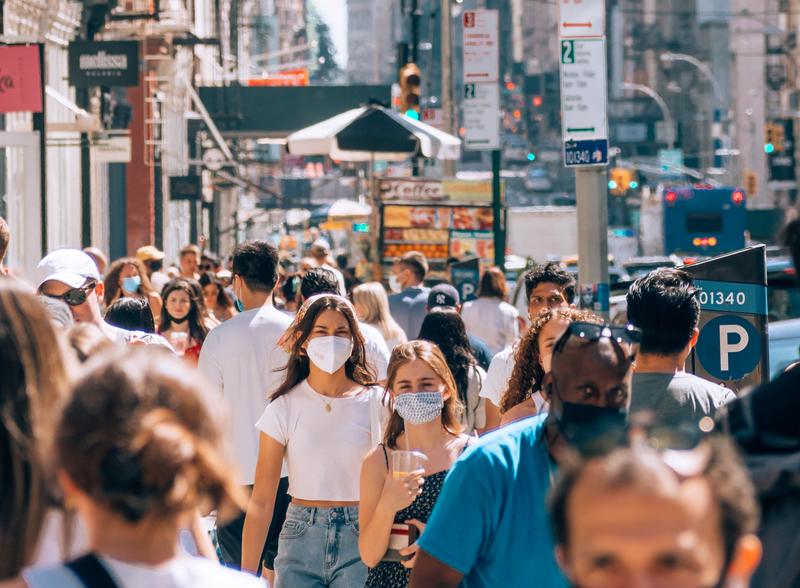People walk along a crowded street, wearing masks