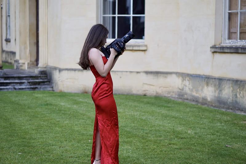 Sarah Brand stands outside holding a camera on the set of her music video