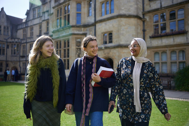 Three students walk across a college lawn in Autumn