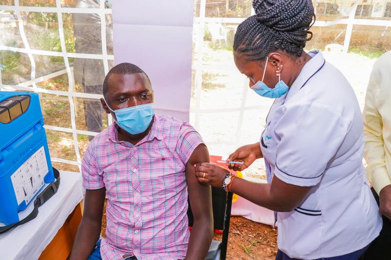 A female nurse gives a man an injection at an outdoor hospital
