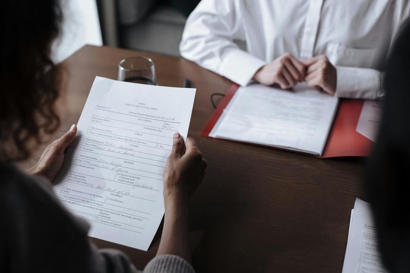 Two people sit opposite each other at a desk, reading documents