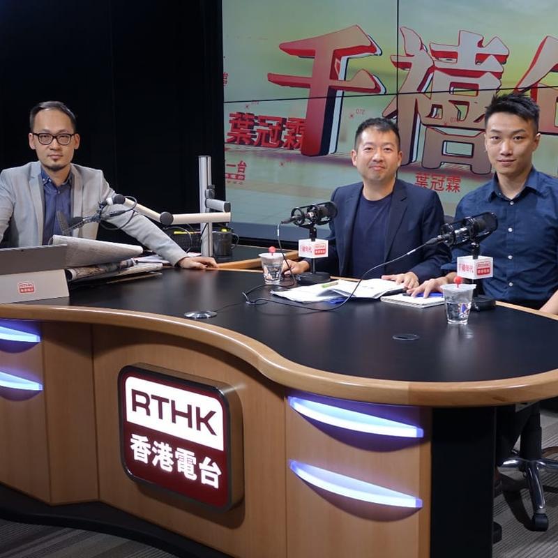 Yiu-tung Suen sits at a television news desk with two men tung