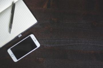 Lined notepad and pen next to iPhone