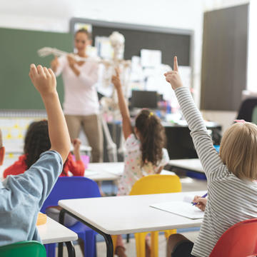 Young children raising their hands in a school classroom