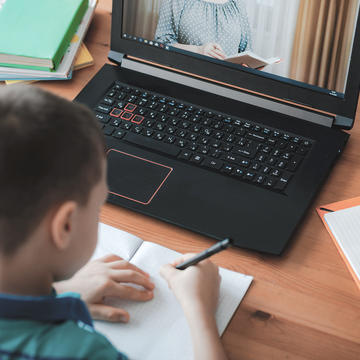 A child taking notes in front of a laptop 