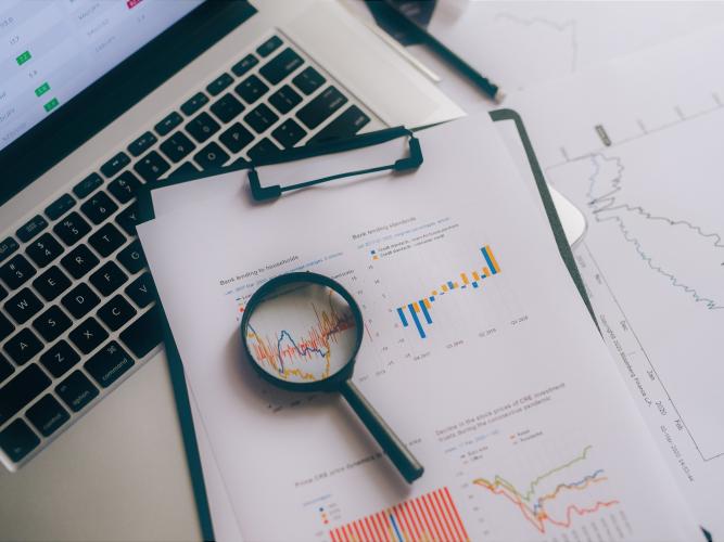A magnifying glass resting on top of graphs and a laptop