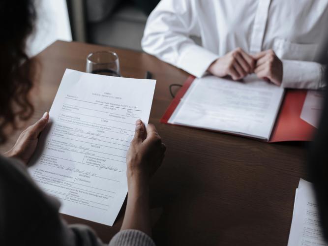 Two people sit opposite each other at a desk, reading documents