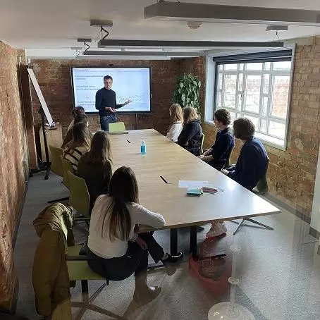 A-Level students sit around a boardroom table while a researcher speaks