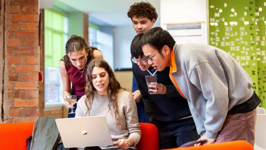 Image of five students looking at a laptop in the Department