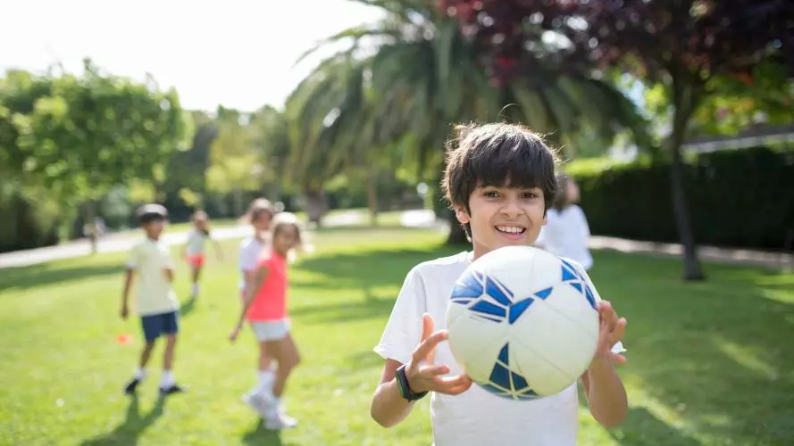 Image of boy holding an football with other children visible in the background 