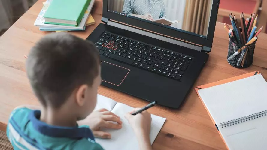 A child taking notes in front of a laptop 