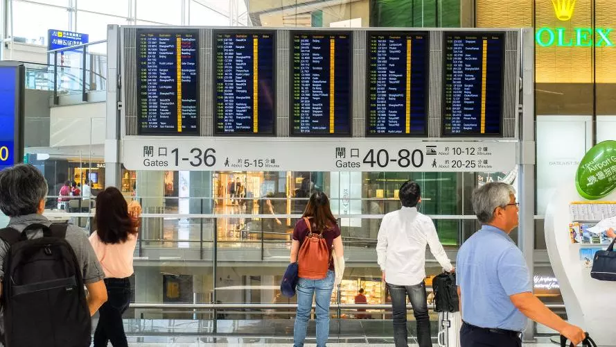 People look at a flight departure board in Hong Kong International Airport
