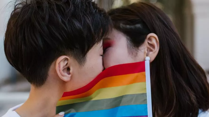 Two women kiss behind a LGBTQ+ pride flag
