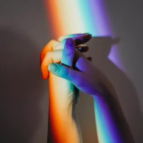 Close-up image of two hands in rainbow coloured light