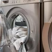 Silver washing machine with towels hanging out of door.