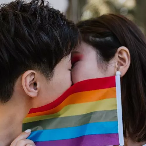 Two women kiss behind a LGBTQ+ pride flag